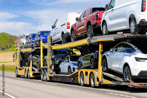 Vehicle carrier truck at speed on road transporting new cars and vans stacked on trailer. 