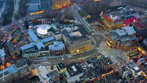 Aerial dusk view of the Leidseplein district in Amsterdam, Netherlands, with the theater square, casino dome, hotels, trams, canal boats and holiday lights on a winter evening.