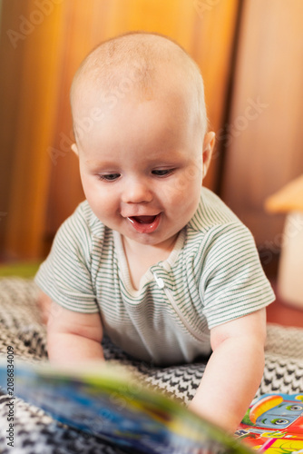 Happy baby in striped onesie looking down at a colorful book