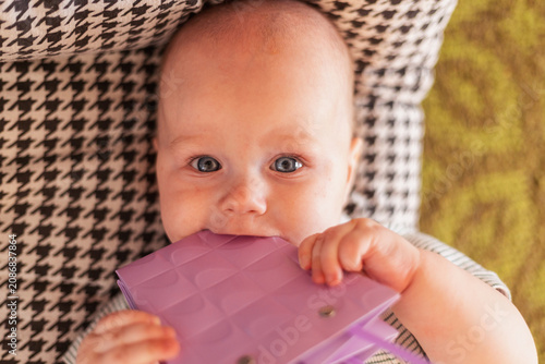 Fotografie Close-up of a baby's face with blue eyes, chewing on a purple toy