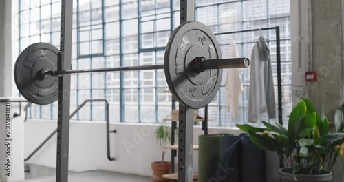 Camera is panning and lowering to showcase mounted barbell with large right plate in loft space