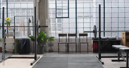 Camera is panning, revealing two squat racks with loaded barbells and bench in gym, showing layout