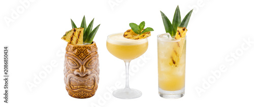 Pineapple cocktail tiki drink tropical beverage set on black background arranged for a summer bar menu, featuring grilled pineapple garnish, mint, and ice in coupe and highball glasses for party vibe