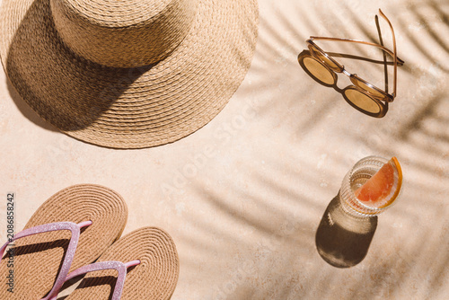 A straw hat, sunglasses, flip-flops, and a refreshing cocktail sit on a sunlit poolside surface with palm shadows, tropical vacation vibe, resort relaxation, luxury lifestyle, summer getaway.
