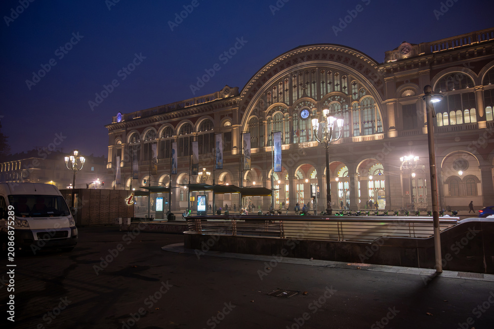 Fototapeta premium Turin, piedmont, italy. November 20, 2024. Turin porta nuova railway station building illuminated at night. Historic architecture with arches and glass reflecting city lights