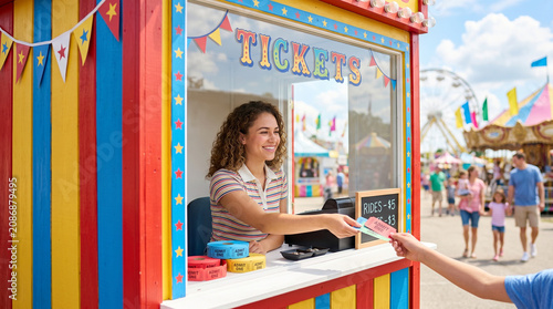 Young woman smiling at carnival ticket booth window and selling tickets  