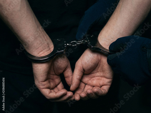 Close up of person hands in metal handcuffs isolated on a dark black background representing crime and arrest