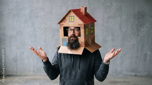 Man wearing a cardboard house on his head with arms outstretched.