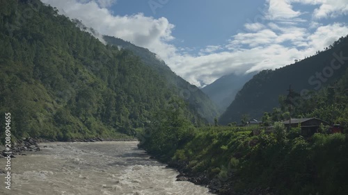 Scenic Mountain Valley View with Fast Flowing Muddy River Under Clouds and Blue Sky