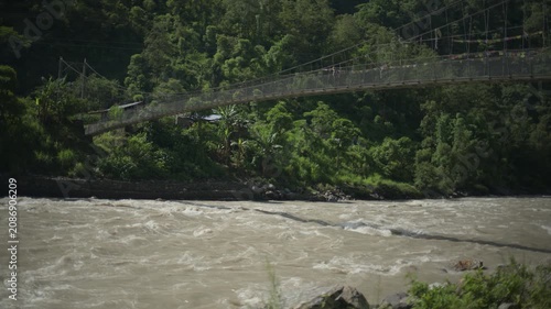 Traditional Mountain Suspension Bridge Crossing Over Fast Flowing Muddy River