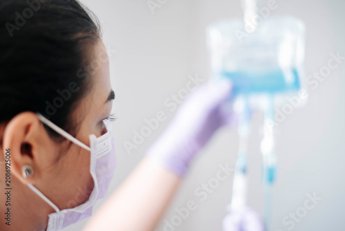 Rear view of a nurse checking an intravenous infusion bag inside a medical clinic.