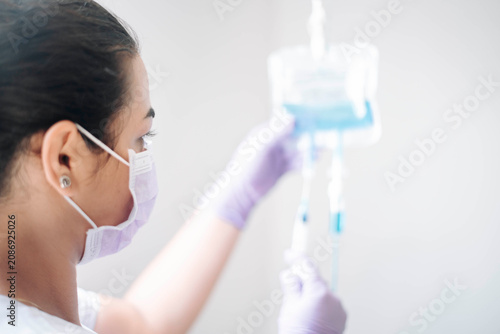 Healthcare worker examining an IV drip bag during intravenous therapy in a clinical environment.