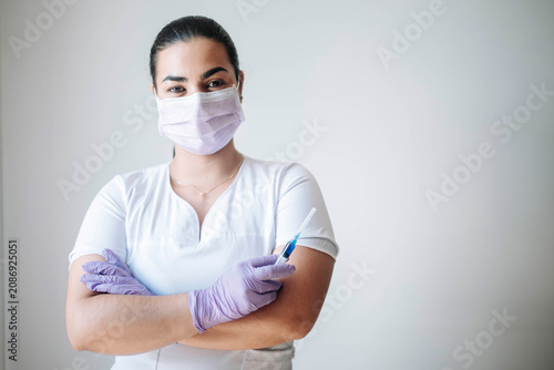 Confident female nurse wearing a face mask and gloves with crossed arms in a modern clinical environment.