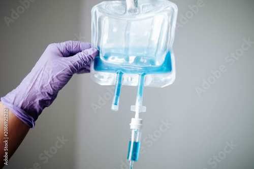 Close-up of a healthcare professional holding an intravenous IV fluid bag in a clinical setting.