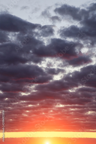 Epic dramatic sunset, sunrise sky with dark fluffy cumulus clouds, orange yellow sun and sunlight background texture