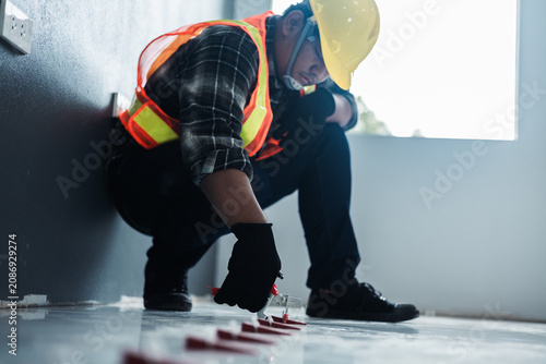 Obraz na płótnie A worker in a safety vest and black gloves uses a tile leveling plier tool to adjust red wedges on a floor, installation and professional interior renovation