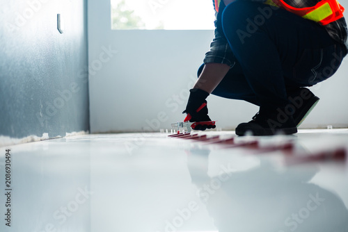 Quadro su tela A worker in a safety vest and black gloves uses a tile leveling plier tool to adjust red wedges on a floor, installation and professional interior renovation