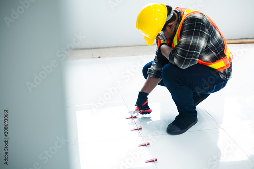 Canvas Print A worker in a safety vest and black gloves uses a tile leveling plier tool to adjust red wedges on a floor, installation and professional interior renovation