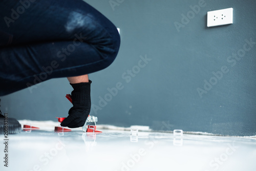 Obraz na płótnie A worker in a safety vest and black gloves uses a tile leveling plier tool to adjust red wedges on a floor, installation and professional interior renovation