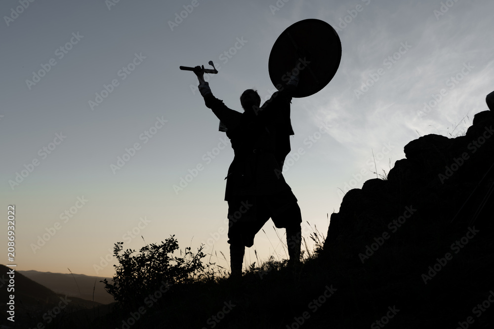 Ταπετσαρία Silhouette of a warrior stands triumphantly against a dusky sky, holding aloft a shield and sword