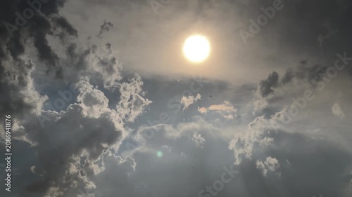 Bright sun glows through breaking storm clouds, casting dramatic beams across moody dark grey sky.