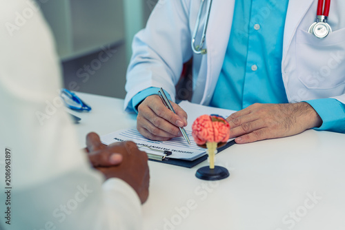 Neurologist discussing brain health and functions with a patient in a clinic.Doctor explaining neurological diagnosis using a human brain model during consultation.