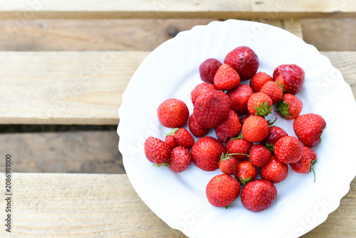 Juicy strawberry on white plate on wooden background, summer time