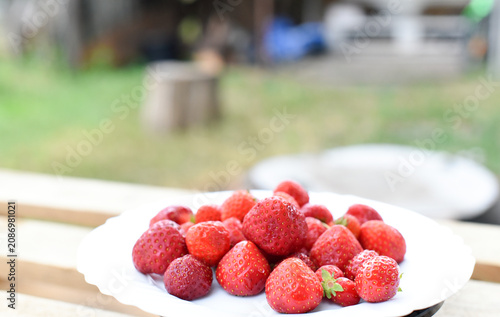 Juicy strawberry on white plate on wooden background, summer time