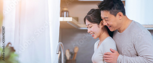 Bild auf Leinwand Smiling Asian Couple Embracing While Cooking Together In Modern Kitchen, Radiating Happiness And Love In Cozy Home Environment