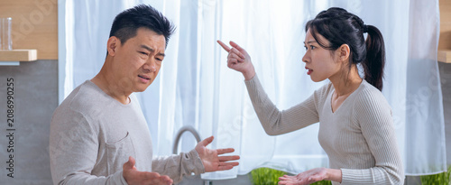 Photos Worried Asian Man And Asian Woman Argue In Kitchen, Woman Pointing Finger While Man Looks Sad