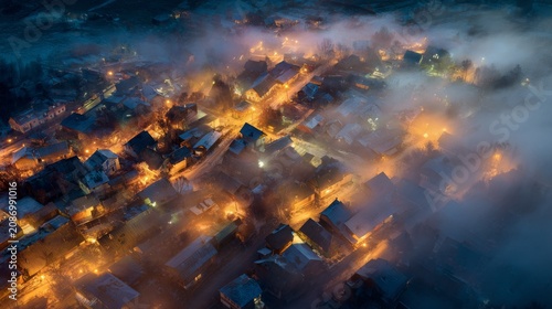 A village at twilight, seen from above, illuminated by warm lights, shrouded in a layer of fog, creating an ethereal glow