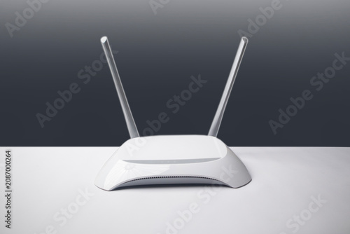 A minimalist white wireless internet router with two antennas, placed on a smooth surface against a gradient grey background.