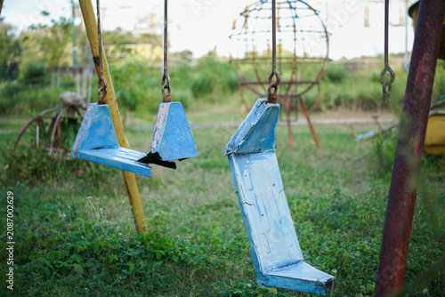 Broken plastic children's swing on the playground, old and unsafe swing. Old blue swing in an abandoned outdoor playground rustic environment