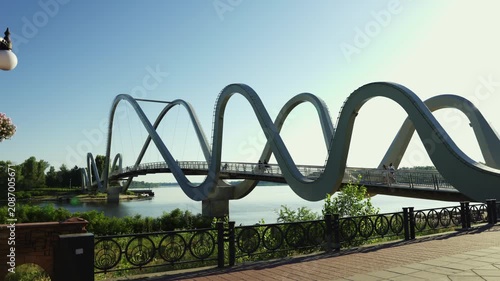 A wide shot of the modern wave pedestrian bridge over the Dnipro river in Kyiv, Ukraine, featuring a futuristic steel design under a clear blue sky on a sunny day