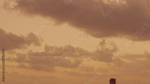 A cinematic shot featuring the top of a person's silhouette moving against a vast, dramatic sunset sky. The focus remains on the texture and color of the clouds with a human element.