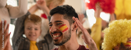 Excited, happy football fans supproting spanish national team in live soccer match at stadium.