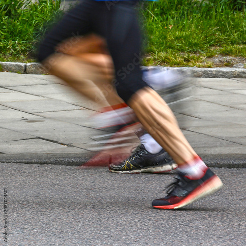 Fotografie Blurred image of runner legs with motion blur beside urban curb during road race