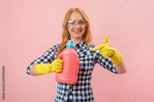 Fotografie Smiling woman wearing yellow gloves and safety goggles holding a bottle of liqui