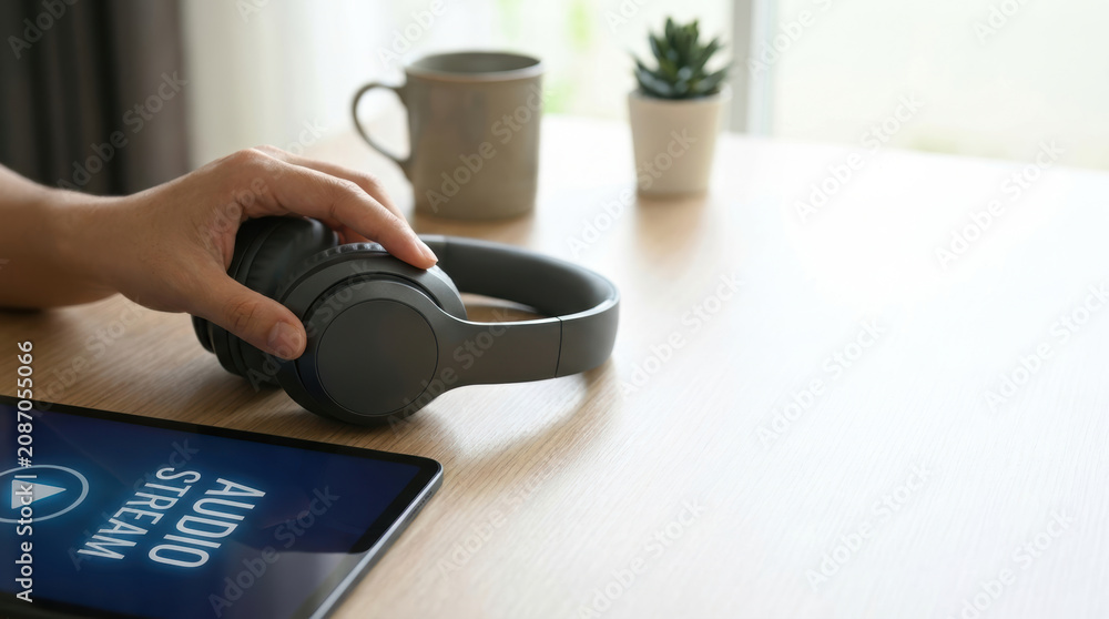 Fototapeta premium Online audio access technology concept with wireless headphones and tablet showing audio stream on wooden table
