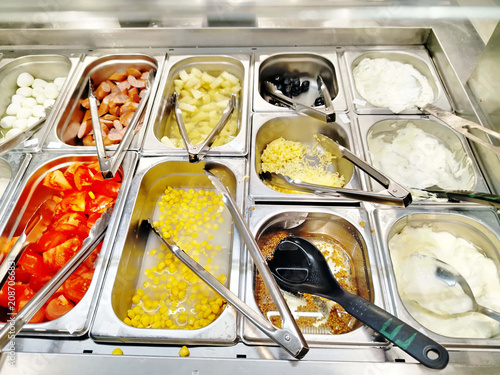Self-Serve Salad Bar Counter With Fresh Toppings Corn Tomatoes Olives Yogurt And Sausage.