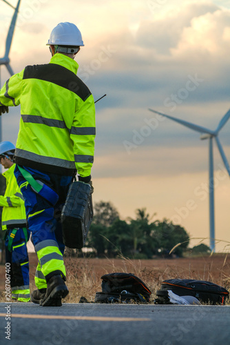 Quadro su tela The wind farm crew of four drift apart and regroup along the pink lit road on the park road under fading skies in pink pastel dusk deep inside a tropical wind energy park