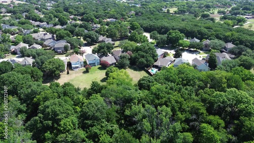 Suburban properties sit alongside sprawling North Texas forest areas. Gray shingle rooftops merge with lush green tree canopies, framing private residential backyards in Flower Mound, Texas