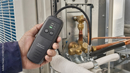 HVAC technician using refrigerant leak detector on outdoor AC unit condenser