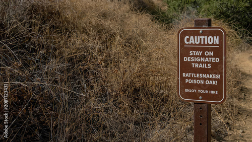 Caution sign on hiking trail warning of rattlesnakes and poison oak in summer