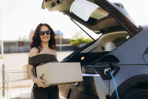 Cuadro en lienzo Woman loading boxes into electric car while charging