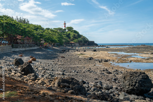 Schilderij op canvas Ba Lang An Lighthouse on forested headland above dark basalt rocks and turquoise