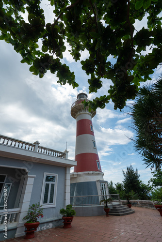 Schilderij op canvas Ba Lang An Lighthouse on forested headland above dark basalt rocks and turquoise