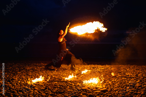 Obraz na płótnie Fire breather performing with a torch on a pebble beach at night