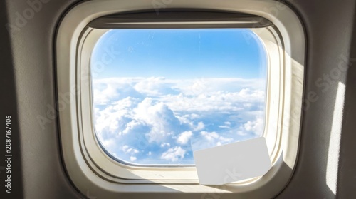 Airplane window view showing a blank white card placed against the glass with a beautiful blue sky and fluffy clouds