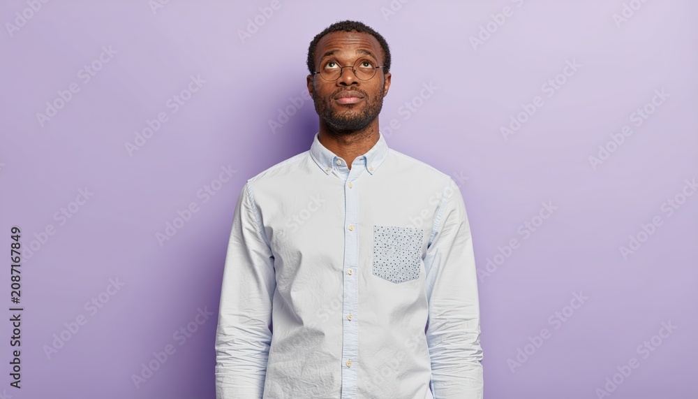 Obraz premium Contemplative african american man looks thoughtfully upwards against soft lavender background
